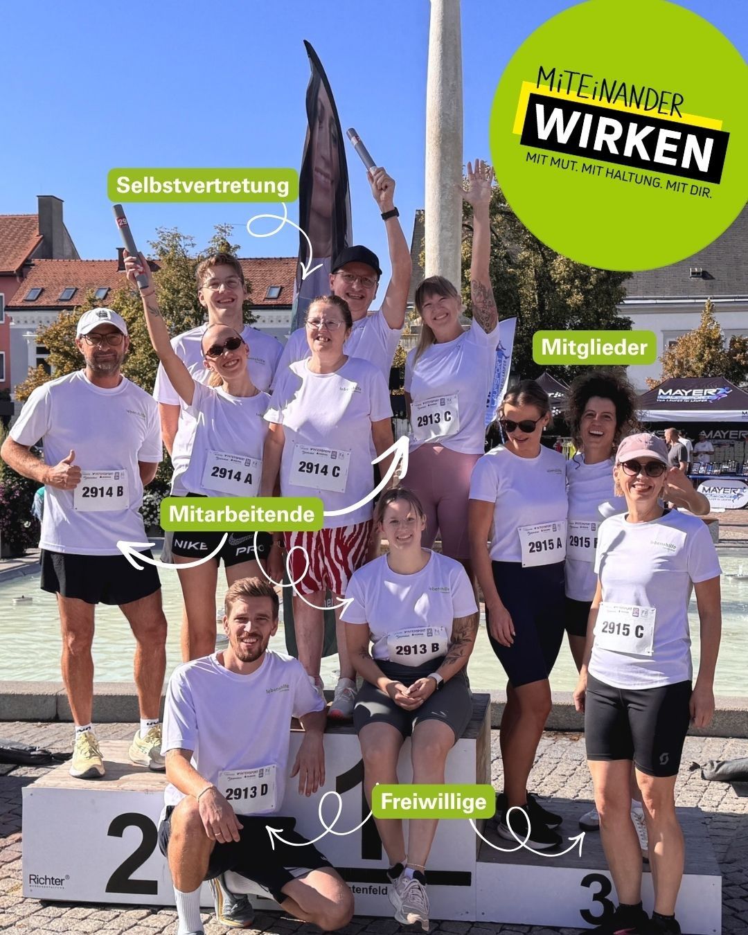 A group of people in white shirts with numbers stand together, smiling and posing for a photo. They are wearing running gear and appear to be celebrating a marathon.