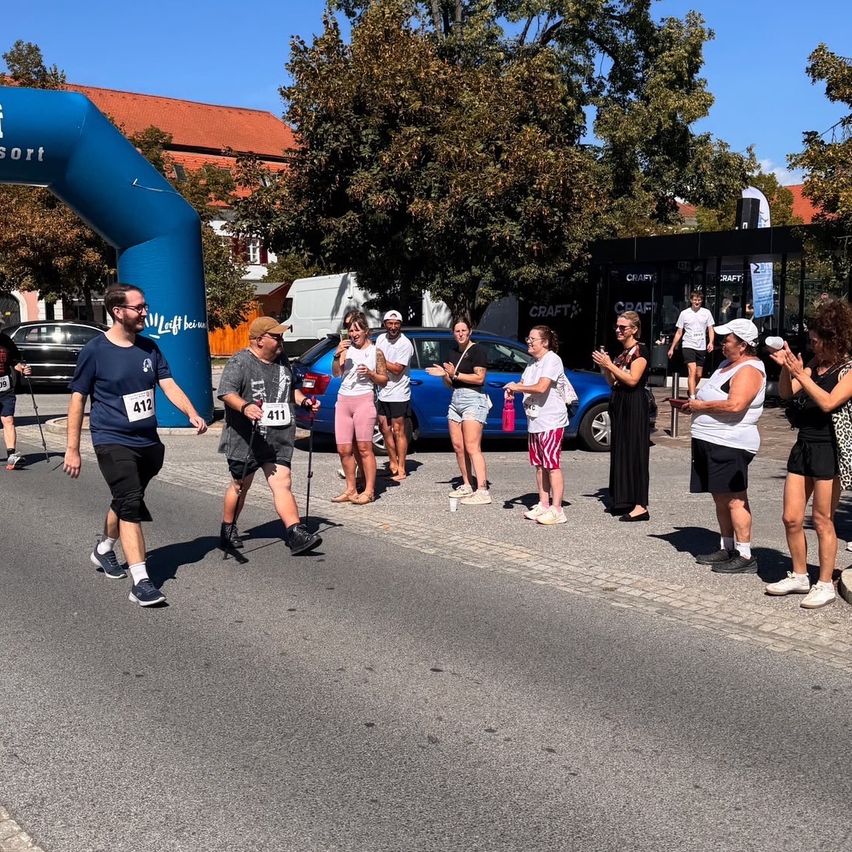 Participants in a marathon cross the finish line, cheered on by spectators. A blue arch marks the finish line.
