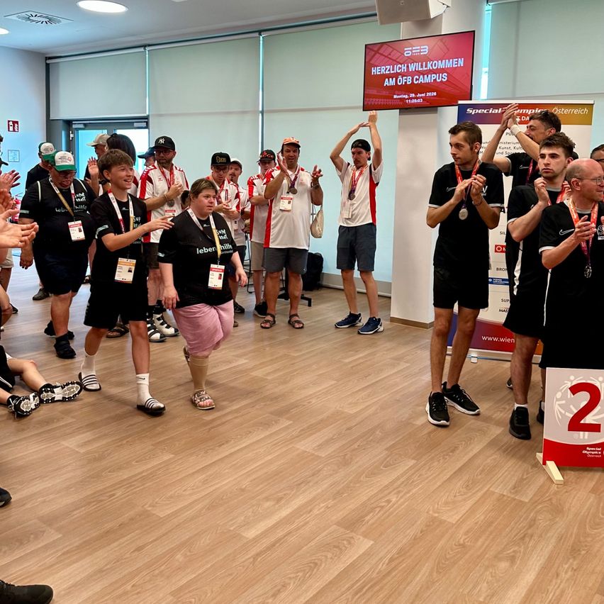 Gruppe von Athleten mit Medaillen und Lächeln bei den Special Olympics, mit einem Schild Herzlich Willkommen am ÖFB Campus.