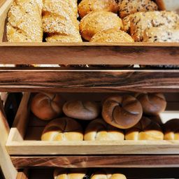 Ein Holztablett hält eine Vielzahl von Brötchen und Buns, darunter sesambestreute und brezelförmige. Sie sind ordentlich gereiht.