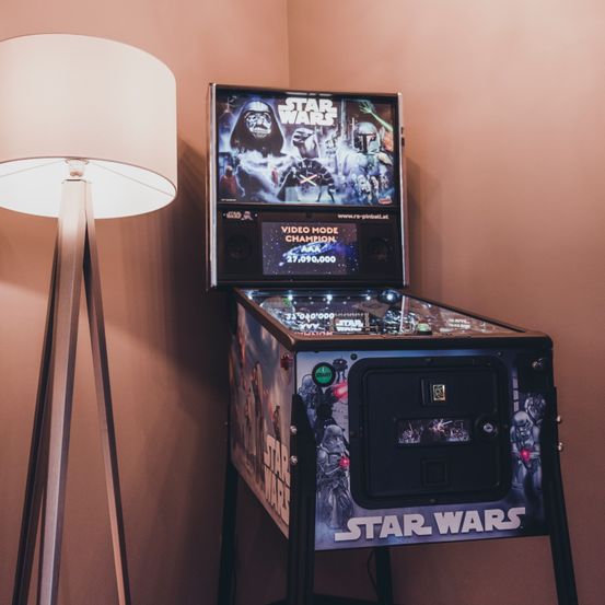 Ein Star Wars Flipperautomat in einer Ecke mit einer Lampe links. Der Bildschirm zeigt eine Szene mit Darth Vader und anderen Charakteren.