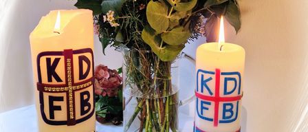 Zwei Kerzen, eine mit der Nummer 25 und die andere mit 35, stehen neben einem Blumenstrauß auf einem weißen Tisch.