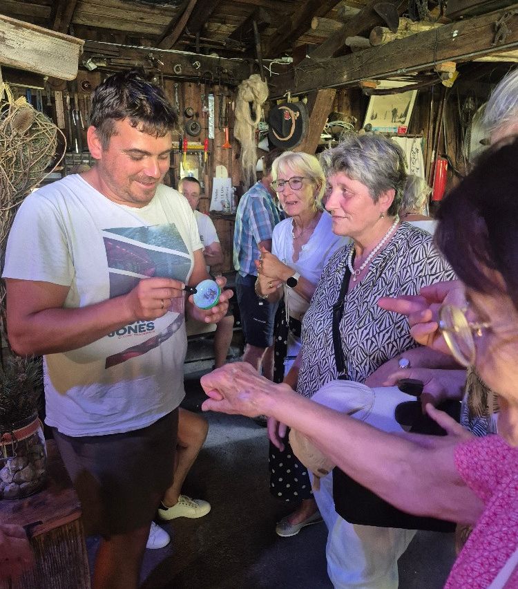 A man in a white shirt and brown shorts is showing a small object to a group of women inside a room.
