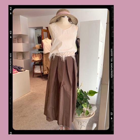 Eine Puppe in einem weißen, ärmellosen Oberteil und einem braunen Rock steht vor einem Spiegel in einem Bekleidungsgeschäft.