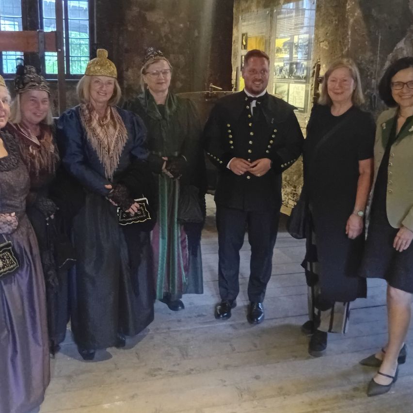 Eine Gruppe von Menschen in historischen Kostümen posiert für ein Foto in einem Raum mit Holzböden und Steinwänden.
