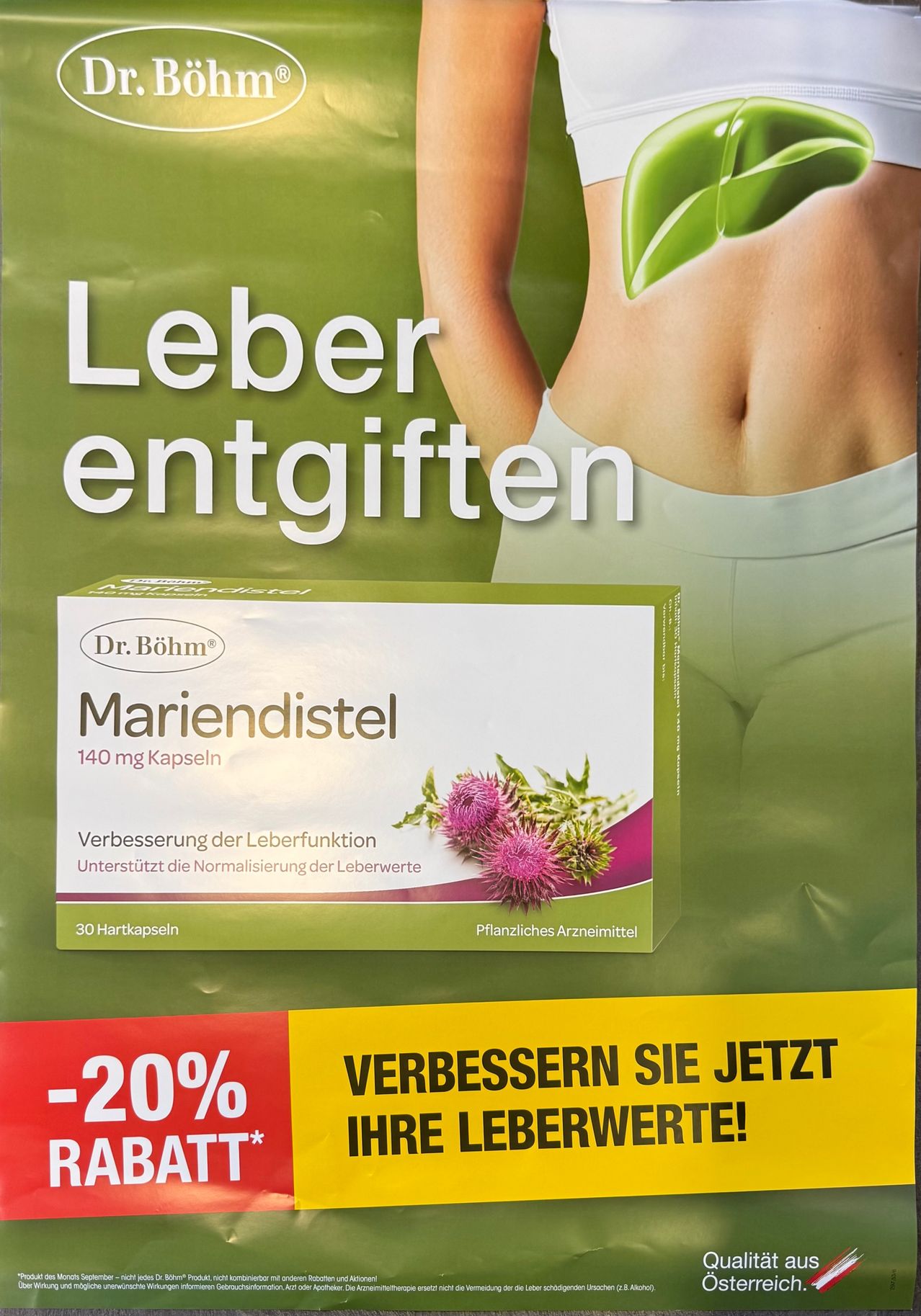Ein Plakat bewirbt Mariendistel 140 mg Kapseln zur Verbesserung der Leberfunktion. Es zeigt eine Frau mit einem grünen Blatt auf dem Bauch und einem Rabattangebot von -20%.