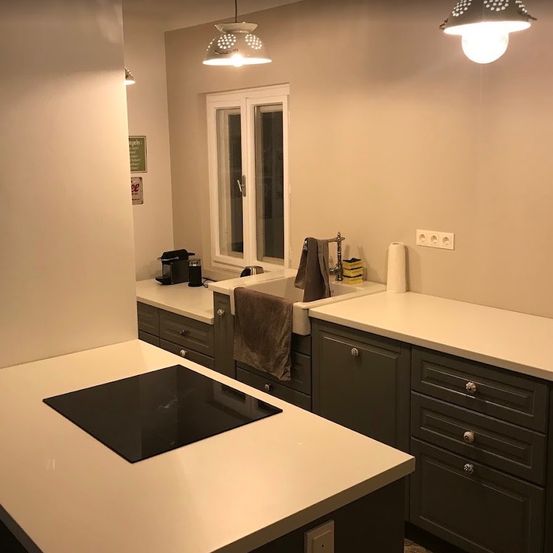 Eine moderne Küche mit weißen Arbeitsplatten, grauen Schränken und einem schwarzen Induktionskochfeld. Ein Waschbecken mit Wasserhahn ist in der Nähe und ein Handtuch hängt an einem Ständer.