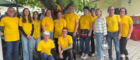 Eine Gruppe von Menschen in gelben T-Shirts posiert für ein Foto im Freien mit Schirmen und einem Baum im Hintergrund.