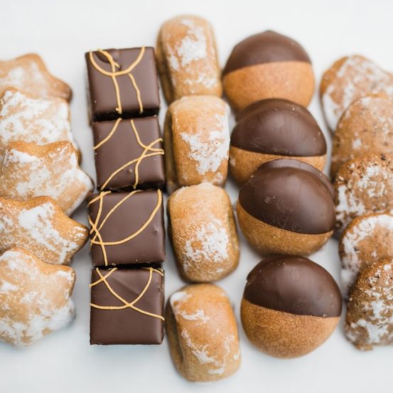 Eine Vielzahl von Gebäckstücken ist auf einer weißen Oberfläche angeordnet. Dazu gehören Schokoladenüberzogene Desserts, sternförmige Kekse und eine Mischung anderer süßer Leckereien.