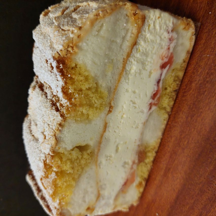 Eine Nahaufnahme eines Kuchenstücks mit cremiger Füllung, knusprigen Kanten und einer Bestäubung mit Puderzucker auf einer Holzoberfläche.