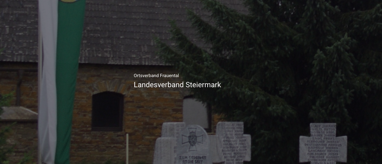Ein Friedhof mit mehreren Grabsteinen ist zu sehen, mit hohen Bäumen im Hintergrund. Die Grabsteine sind verwittert und haben deutsche Inschriften.