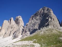 Eine raue Bergkette mit steilen Klippen und felsigem Gelände. Grüne Grasflecken säumen die Landschaft gegen einen klaren blauen Himmel.