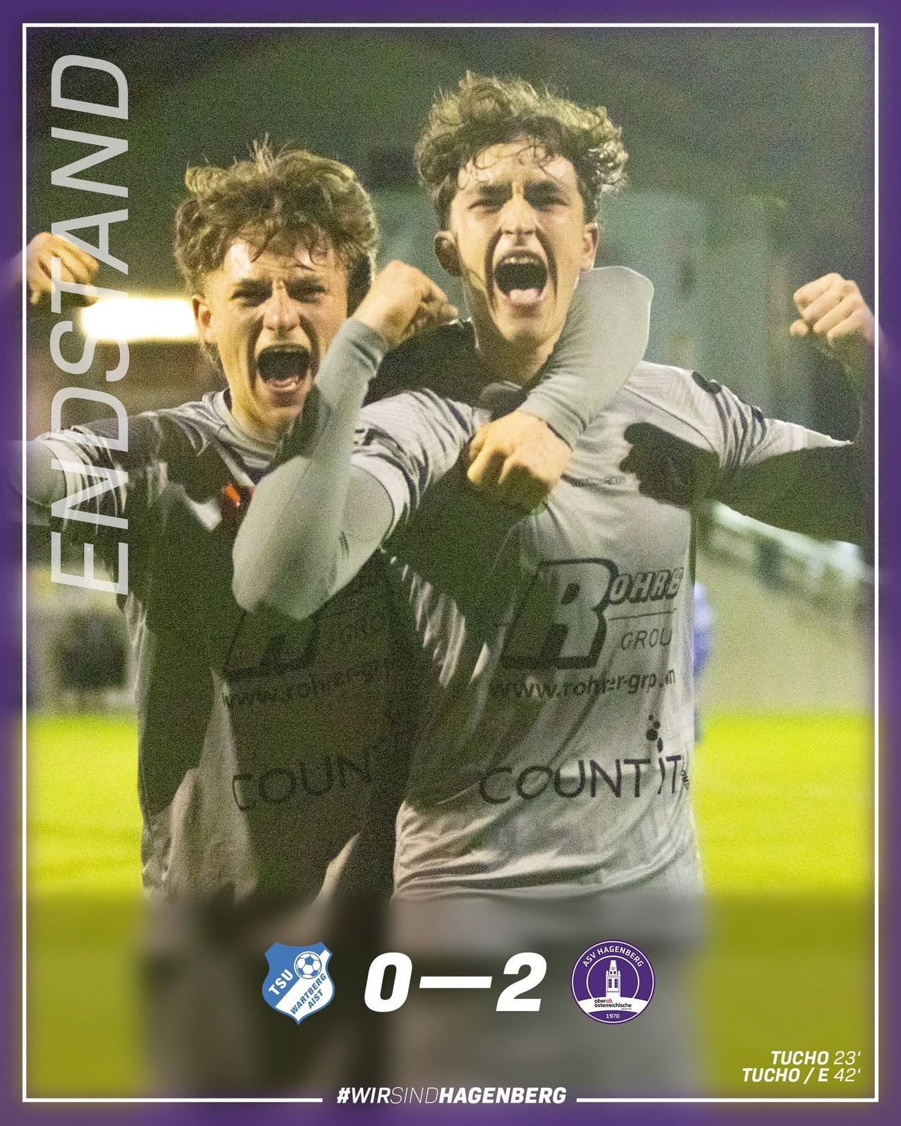 Zwei junge Fußballspieler feiern einen Sieg mit einem Ergebnis von 0-2, stehen auf einem Feld, wobei einer den anderen von hinten umarmt.