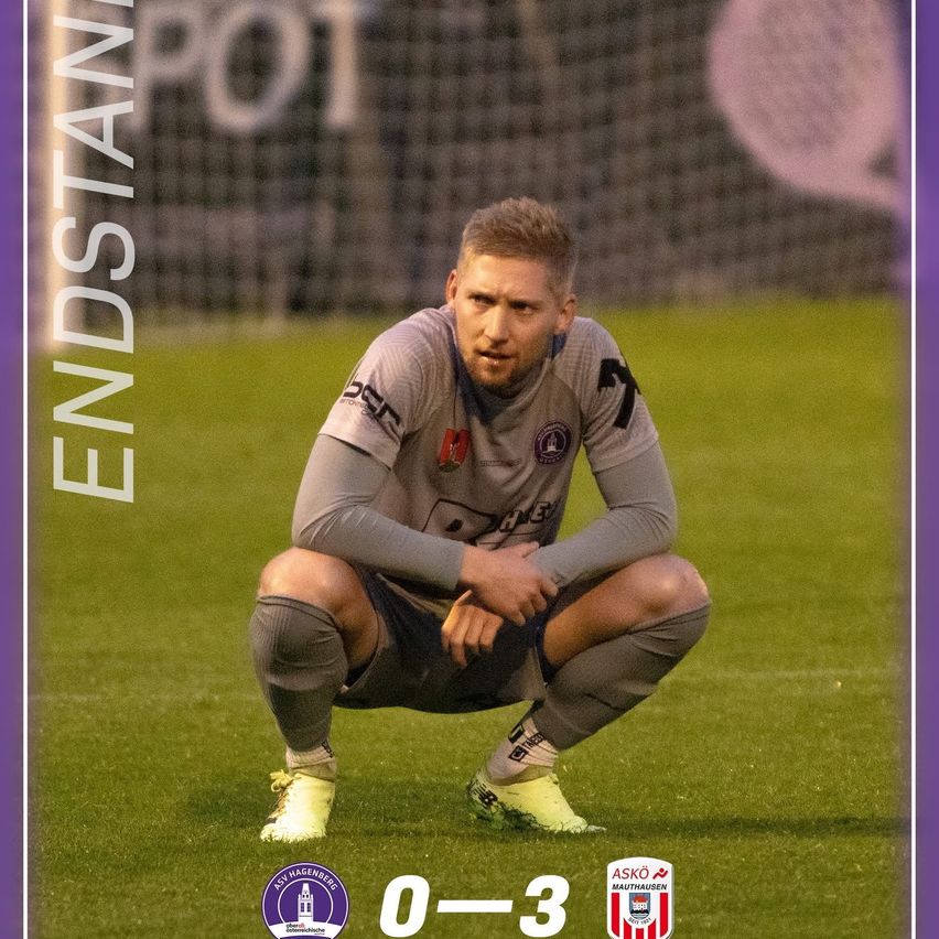 A soccer player kneels on the field, looking downward, with a scoreboard showing 0-3 in the background. He wears a gray jersey.