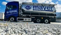 Ein blauer Mayer-Lkw mit einem großen silbernen Tank steht auf einer Schotterstraße mit Bergen im Hintergrund.