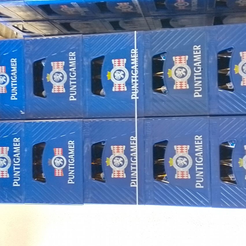 Ein Stapel blauer Schachteln mit der Aufschrift 'PUNTIGAMER' und einem Emblem, möglicherweise mit Produkten gefüllt. Die Schachteln sind ordentlich in einer Reihe angeordnet.