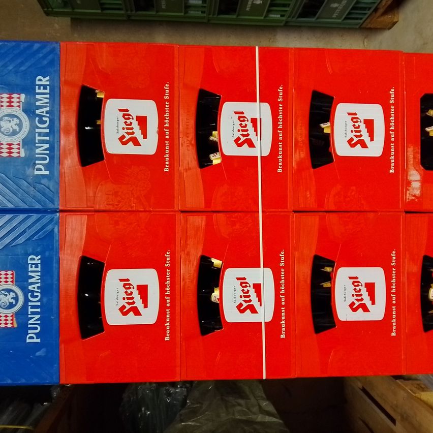 Mehrere rote Schachteln mit einem weißen Logo, das mit Stiegl gekennzeichnet ist, sind in einer Reihe gestapelt. Die Schachteln haben schwarze zylindrische Formen auf der Oberseite. Die Schachteln sind mit 'Puntigamer' und 'Frühstück auf einem höheren Niveau' gekennzeichnet.
