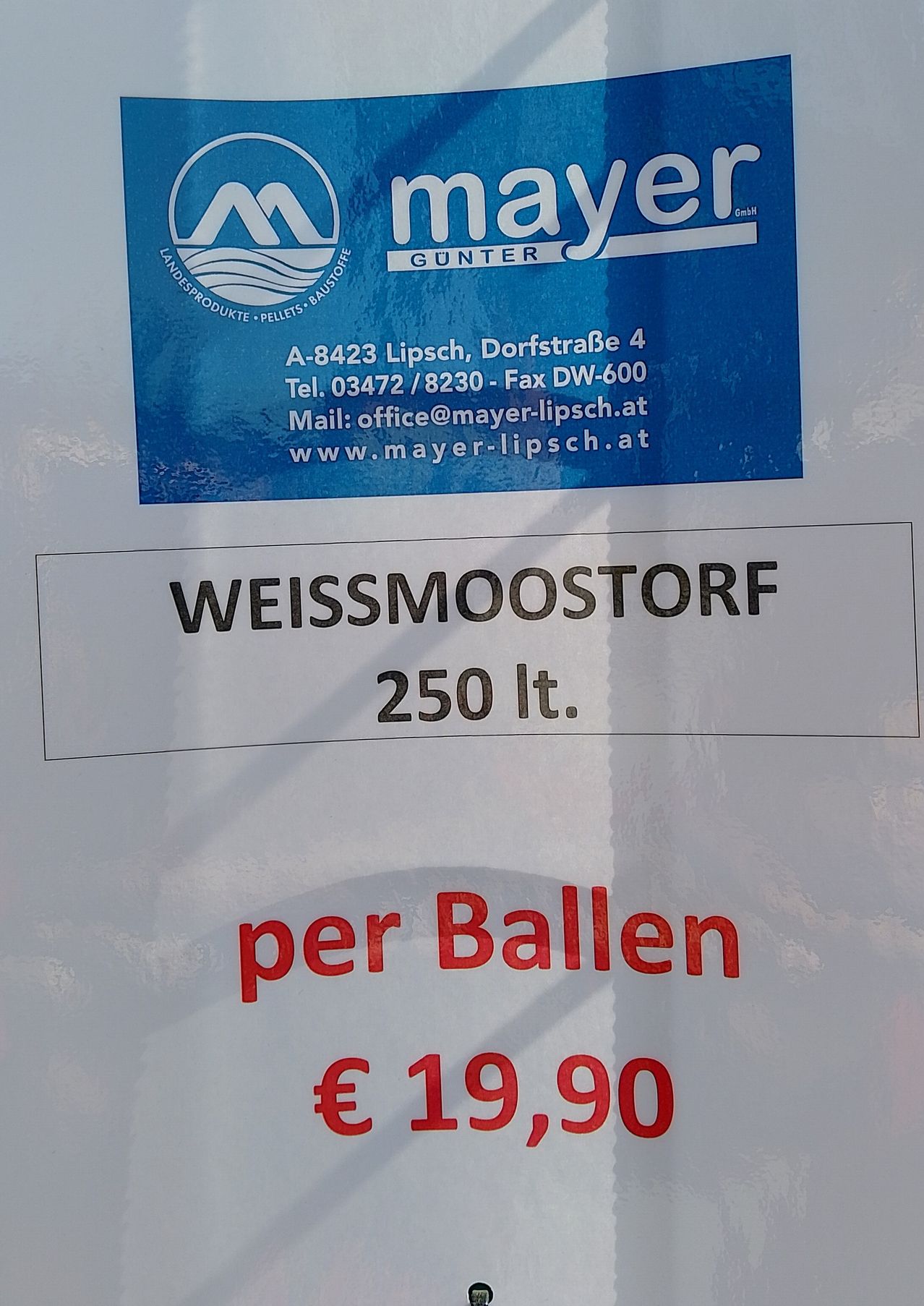 Ein blaues Schild von Mayer Gunter zeigt Kontaktdaten und Produktdetails. Darunter steht auf einem weißen Etikett Weissmoostorf, 250 Liter, pro Ball und kostet 19,90 €.