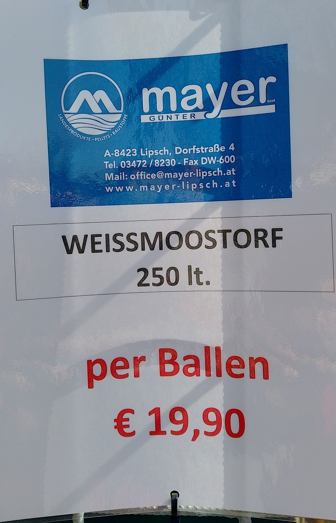 Ein blaues Schild von Mayer Gunter zeigt Kontaktdaten und Produktdetails. Darunter steht auf einem weißen Etikett Weissmoostorf, 250 Liter, pro Ball und kostet 19,90 €.