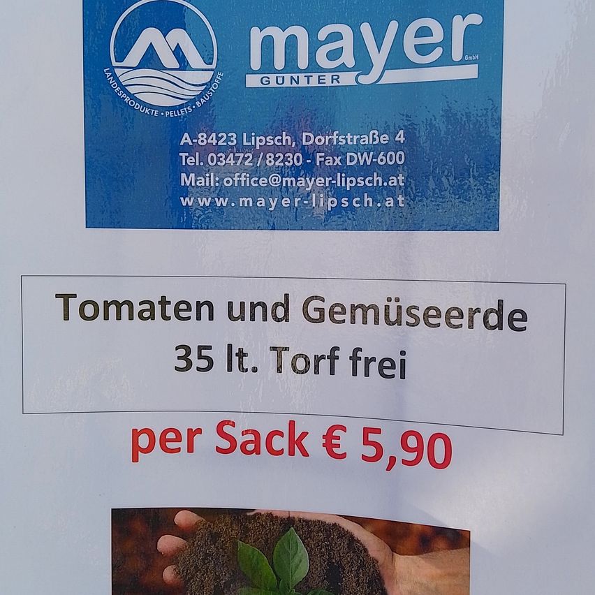 Ein blaues Schild mit dem Logo von Mayer GUNTNER. Kontaktdaten umfassen Adresse, Telefonnummer, Faxnummer, E-Mail und Website. Darunter steht ein Hinweis über Tomaten und Gemüsesamen, 35 Liter frei pro Sack, zum Preis von 5,90 €.