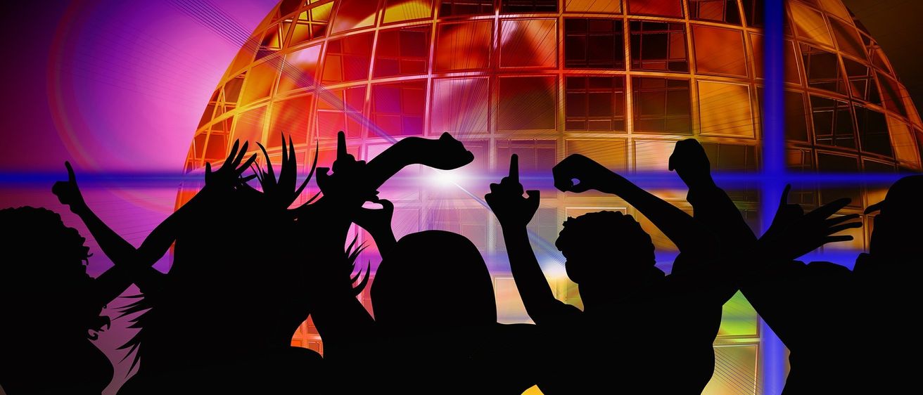 Eine Gruppe von Menschen tanzt in einem farbenfrohen, lebhaften Disco mit einer großen Discokugel im Hintergrund.