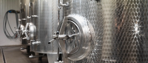 Edelstahl-Weintanks in einem Weinkeller mit mehreren Ventilen und einem offenen Verschluss.