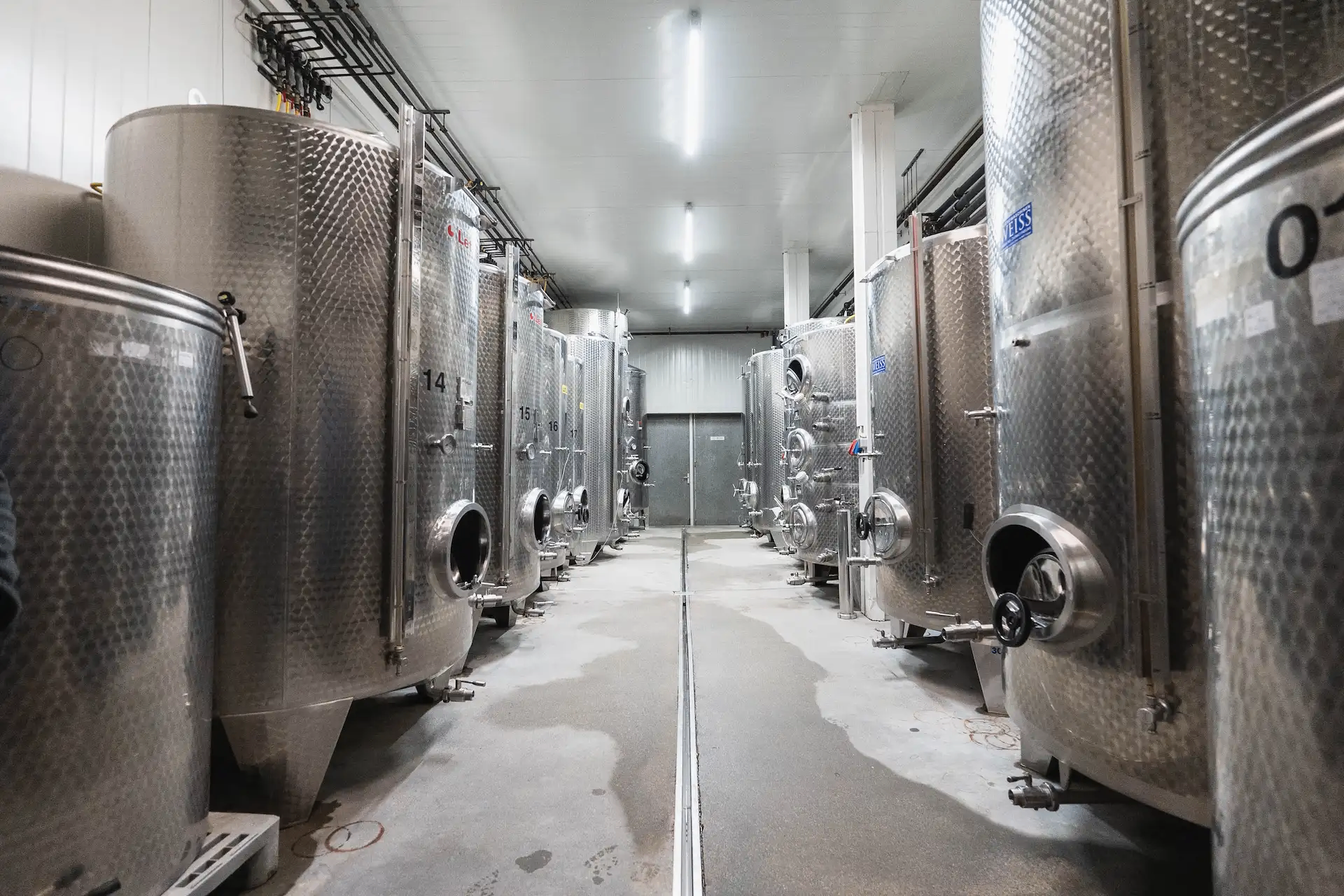 Große Edelstahltanks mit den Bezeichnungen 14 und 15 stehen in einer Fabrik mit weißer Decke und grauem Boden in einer Reihe.