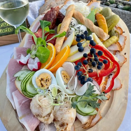 Ein Holzbrett mit verschiedenen Fleischsorten, Gemüse, Eiern und einem Glas Wein auf dem Tisch.