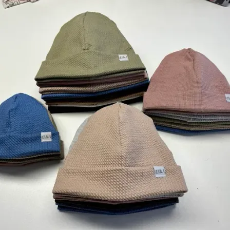 Eine Sammlung von gestrickten Mützen in verschiedenen Farben ist ordentlich auf einer weißen Oberfläche gestapelt, einschließlich Blau-, Rosa- und Beigetönen.