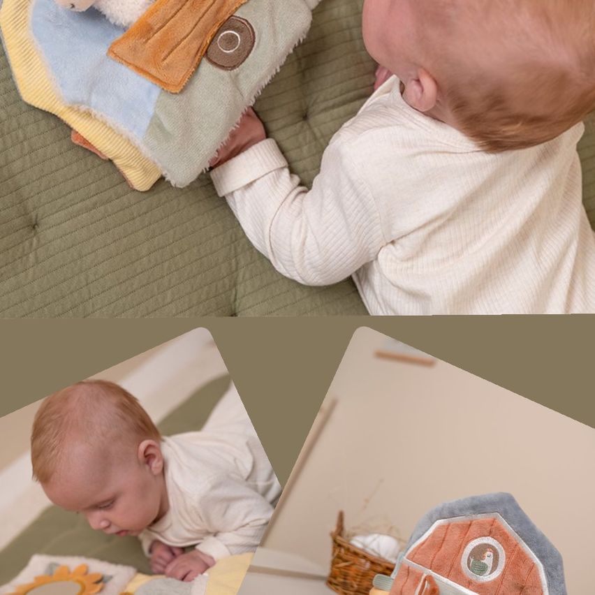 Ein Baby liegt auf einem Bett und spielt mit einer mehrfarbigen Decke mit einem Tier und einem Sonnenspiegel. Das Baby trägt ein weißes Langarmshirt.
