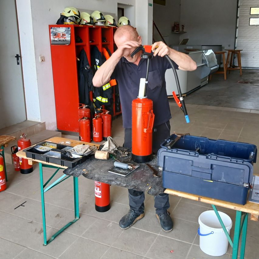 Ein Mann in einem Raum mit Feuerlöschern hält einen roten Feuerlöscher mit den Händen und überprüft ihn.