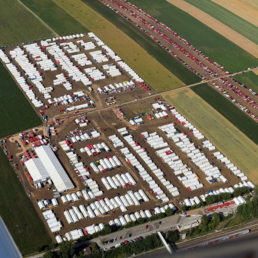 Eine Luftaufnahme eines riesigen Flüchtlingslagers mit Reihen von Zelten, einige in Rot, in einem grünen Feld mit verstreuten Fahrzeugen und Straßen.