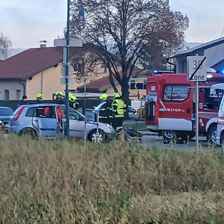Rettungskräfte kümmern sich um einen Autounfall auf einer Straße mit Gebäuden und einem Geschwindigkeitsschild in der Nähe.