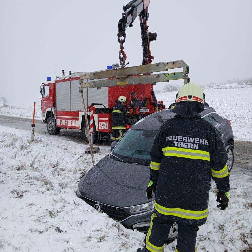 Feuerwehrleute benutzen einen Kran, um ein Auto aus dem Schnee auf einer verschneiten Straße zu ziehen. Das Auto ist halb im Schnee vergraben.