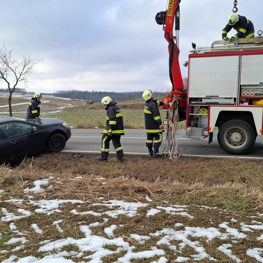 Firefighters are rescuing a car from the side of the road. Four firefighters are present, two on the truck and two on the ground. The car is on its side with the front end damaged.