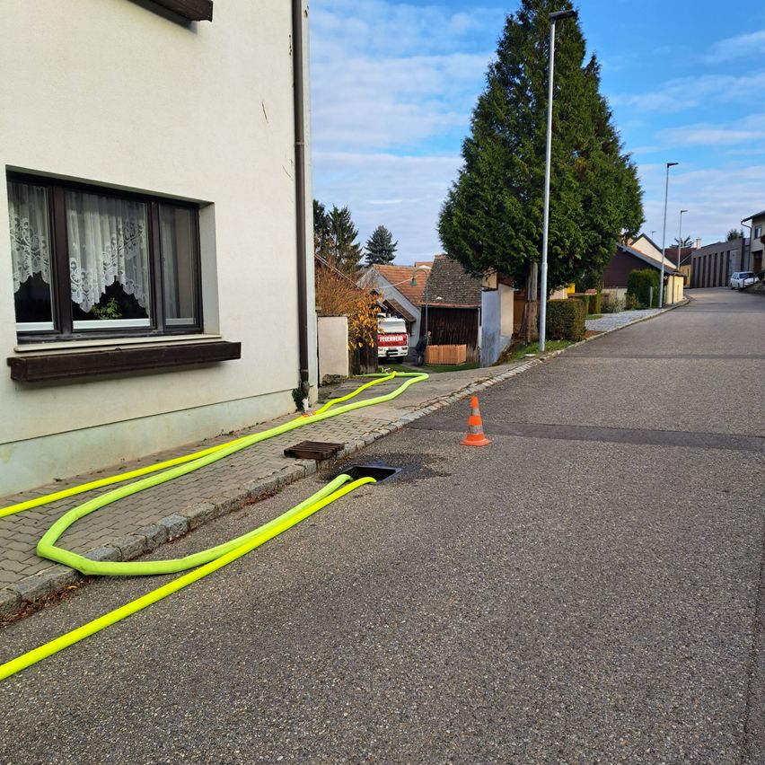 An empty street with yellow pipes and an orange traffic cone. A building with a window and a white car is parked on the side.