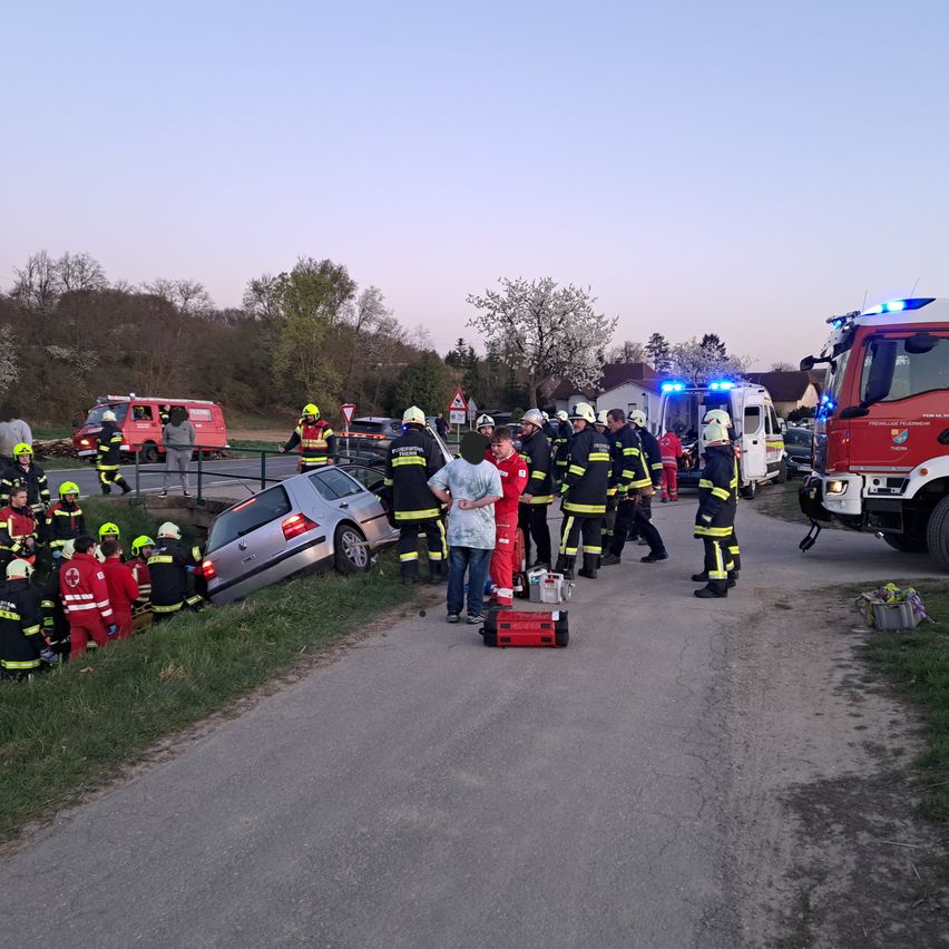Einsatzkräfte stehen um ein umgekipptes Auto am Straßenrand. Mehrere Feuerwehrfahrzeuge sind anwesend, und Personal kümmert sich um den Unfall.