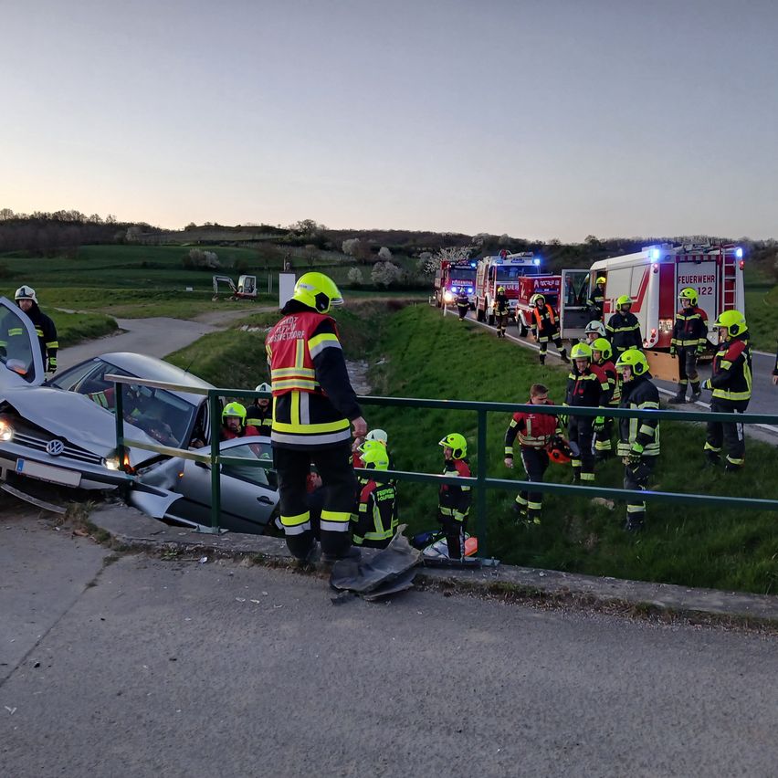 Feuerwehrleute in Schutzausrüstung helfen bei einem Unfall. Ein Auto ist halb im Graben versunken, während andere in der Nähe geparkt sind.
