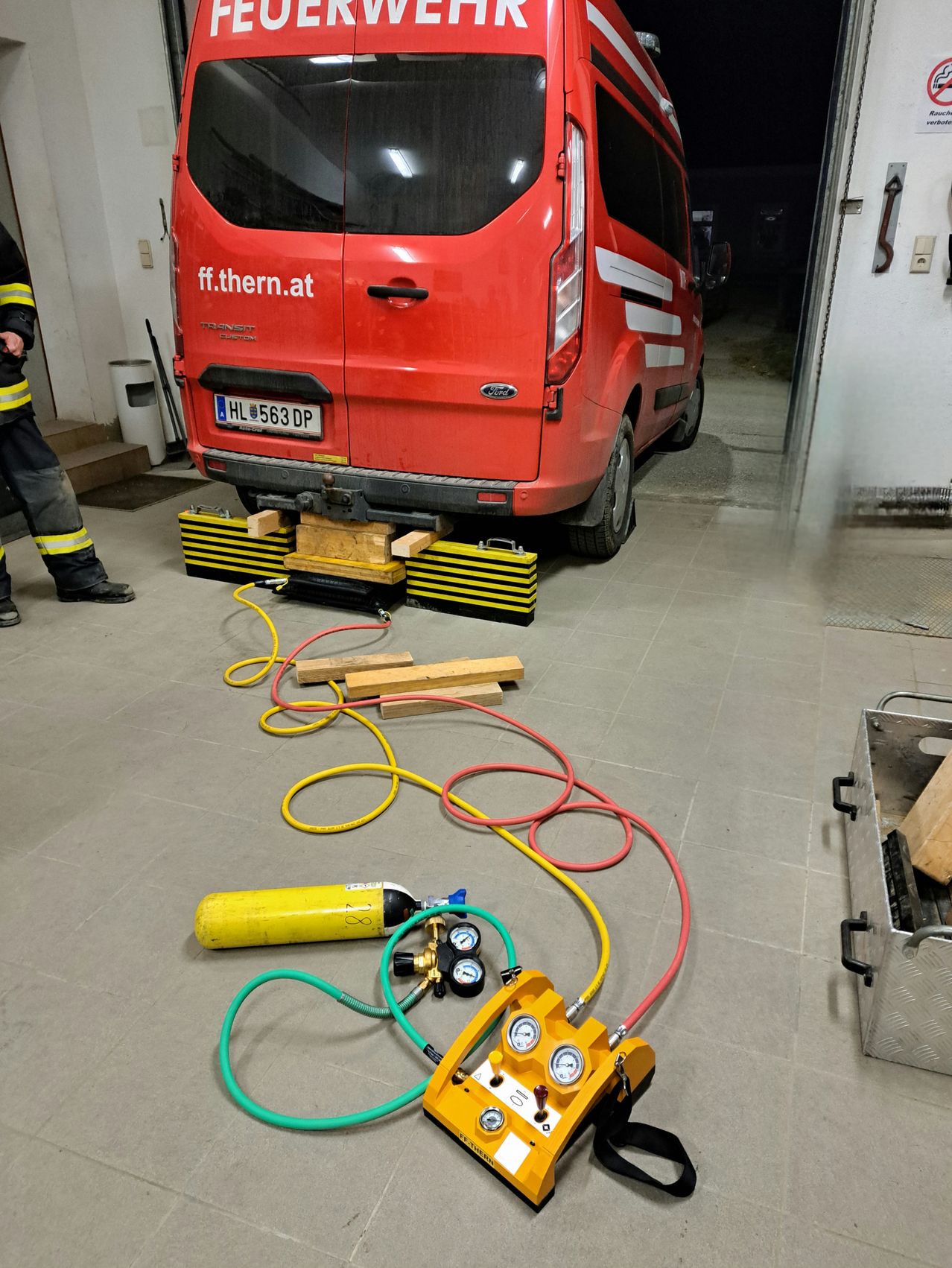 A red van with the license plate HL 563 DP is parked in a garage, with a yellow cylinder and various tools and hoses on the floor.