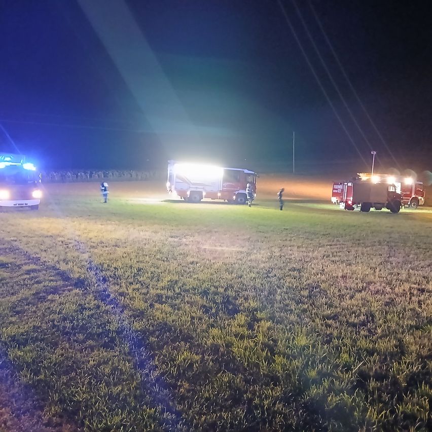 Feuerwehrleute sind nachts mit Einsatzfahrzeugen und Lichtern in einem offenen Feld mit einem Vorfall beschäftigt.