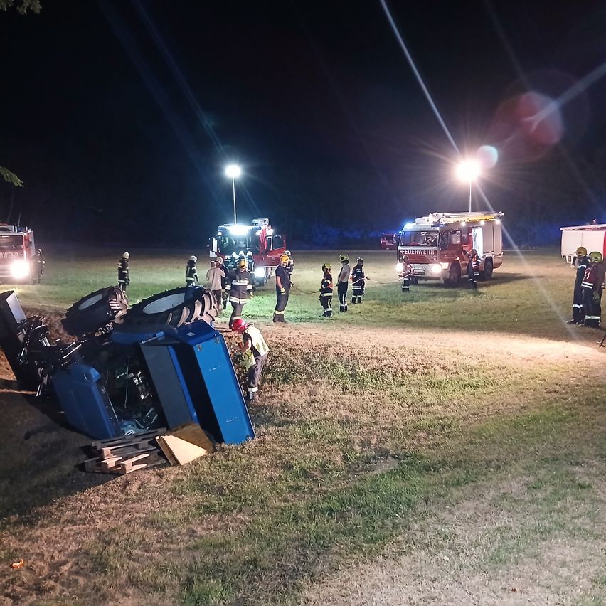 Feuerwehrleute kümmern sich um einen Verkehrsunfall bei Nacht. Das Fahrzeug ist auf dem Rasen umgekippt.