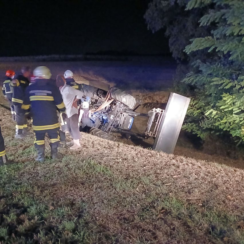 Feuerwehrleute retten eine Person aus einem umgekippten Fahrzeug bei Nacht. Sie tragen Helme und Uniformen.