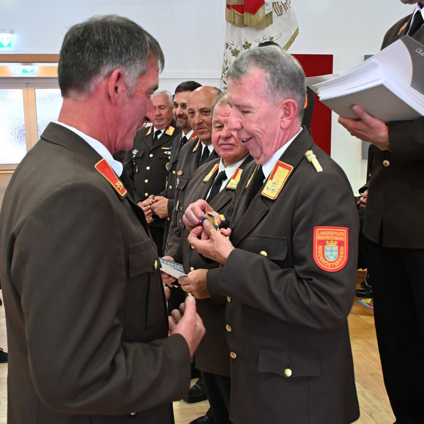 Militärbeamte in Uniform tauschen eine Medaille aus. Der Mann, der die Medaille erhält, lächelt.