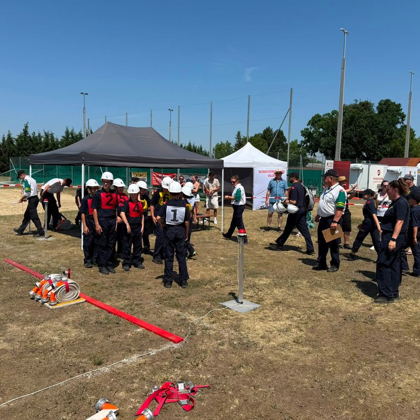 A group of people in uniforms and helmets are gathered in an outdoor area. Some are standing and some are walking. There are tents, fire extinguishers, and wires on the ground.