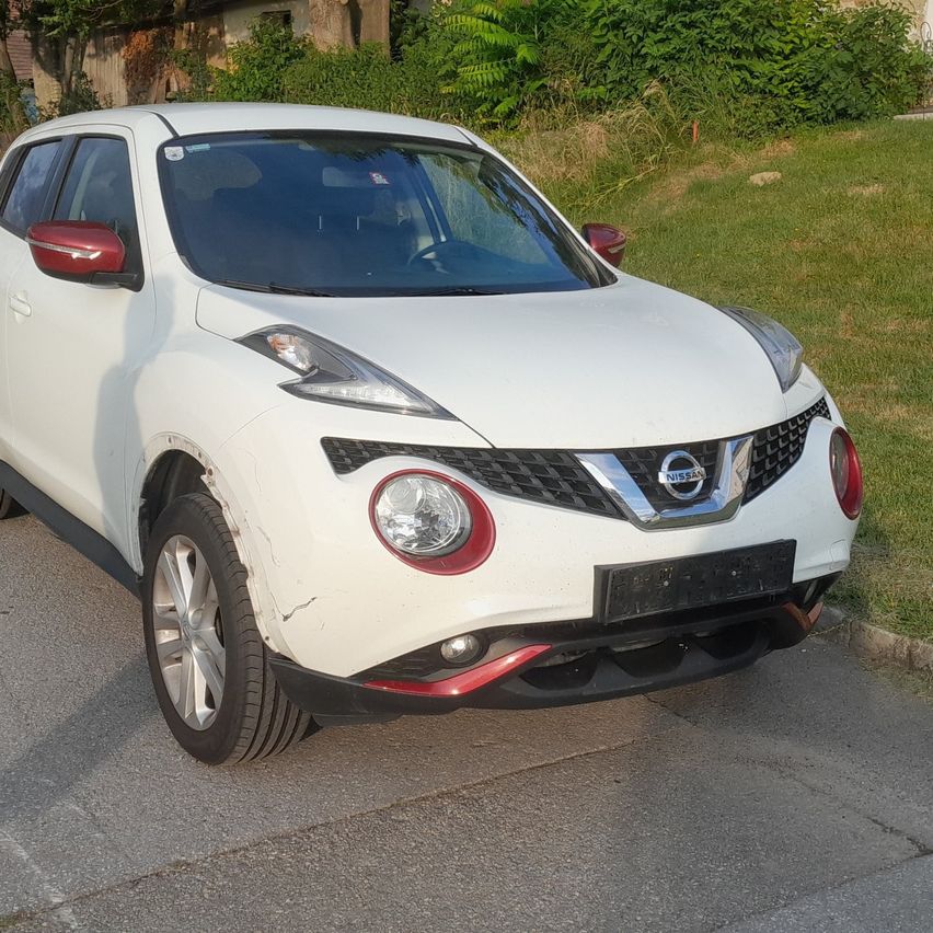 A white Nissan Juke is parked on the side of a road. It has red trims and a black bumper.