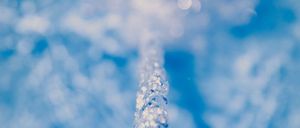 Eine Nahaufnahme eines Wassertropfens, der von einem Wasserhahn in einen Pool fällt, dabei Wellen schlägt und unter dem Licht funkelt.