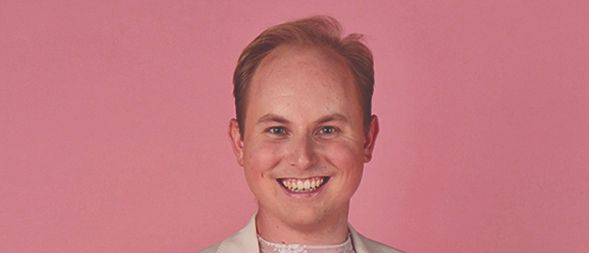 A smiling man wearing a beige suit jacket over a pink lace top poses on a pink background. The text reads Adrenalin Die Julian Weniger Show 15.11.2025 Ghega Halle Payerbach.