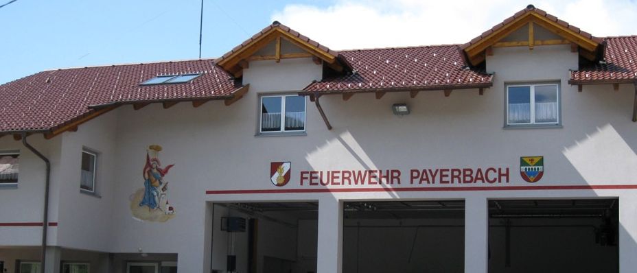 Eine Band spielt vor dem Feuerwehr Payerbach-Gebäude, vor dem sich eine Menschenmenge versammelt hat. Das Gebäude hat rote Dächer und zwei große Garagentore.