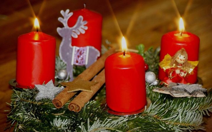 Vier rote Kerzen sind in einem Kranz aus Tannennadeln entzündet, geschmückt mit Zimtstangen, silbernen Sternen und einer Rentierfigur.
