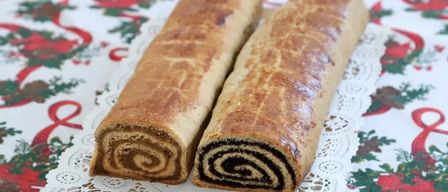 Zwei Schokoladenrollen sind auf einer weißen Spitzenunterlage auf einem weihnachtlich gestalteten Tischtuch ausgestellt.